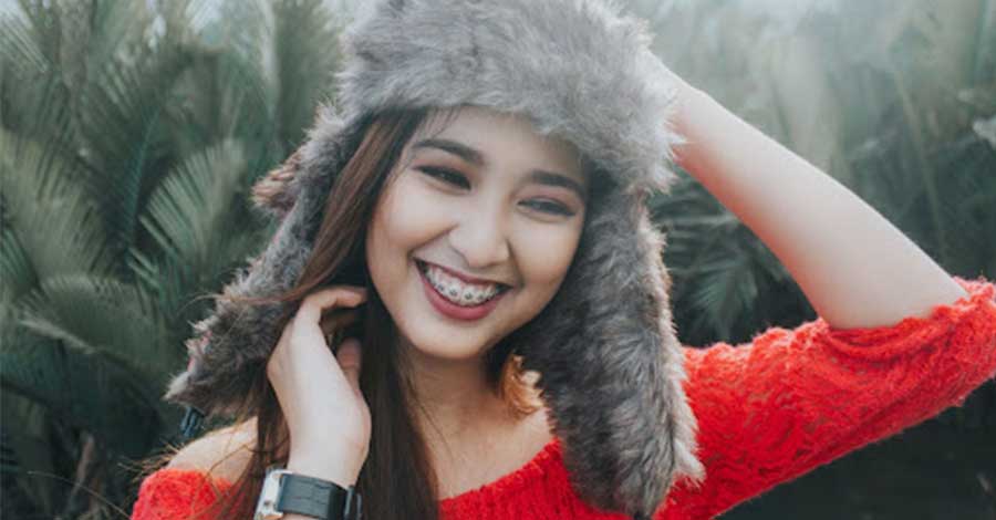 A photo of a smiling woman in red tops wearing a beanie.